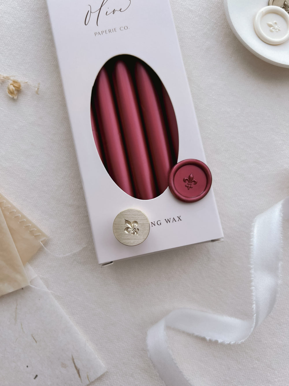 dark metallic red mini fleur de lis wax seal and a brass stamp head on a box of metallic red sealing wax sticks