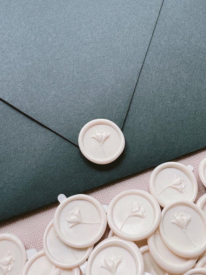 Off-white mini flower wax seal stickers on a dark green envelope