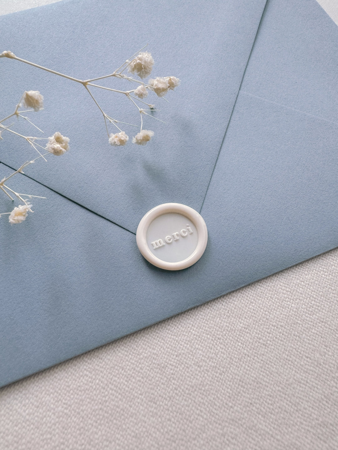 Antique white mini merci wax seal on a dusty blue envelope on a light beige background