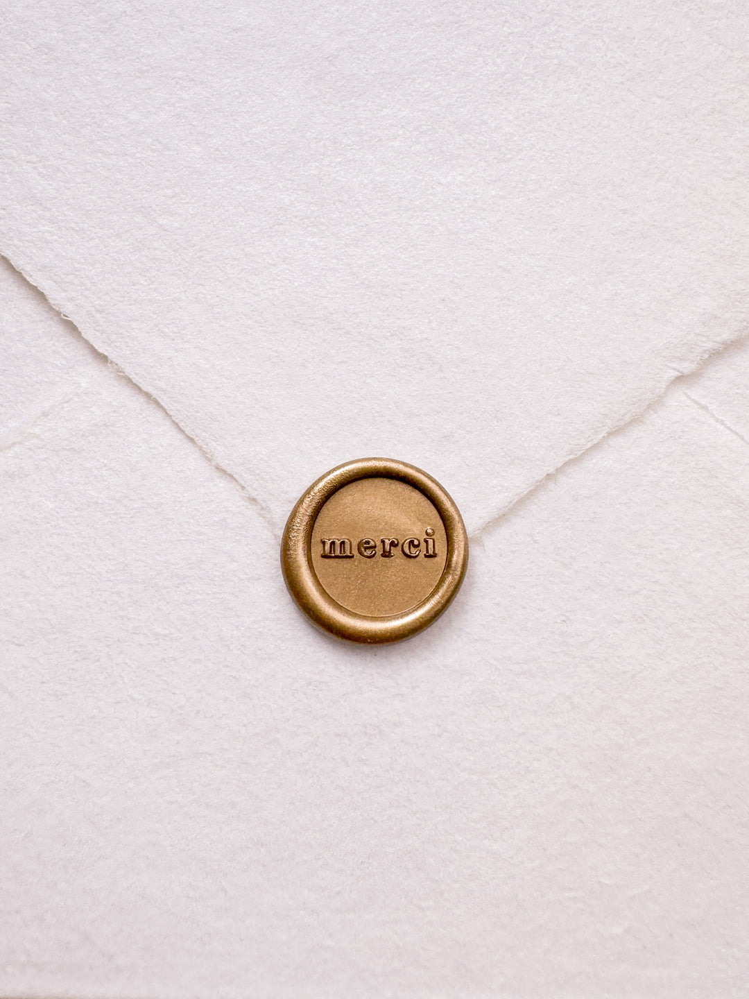 Gold mini merci wax seal on a white deckled edge handmade paper envelope