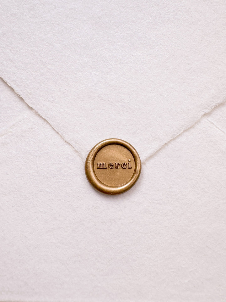Gold mini merci wax seal on a white deckled edge handmade paper envelope