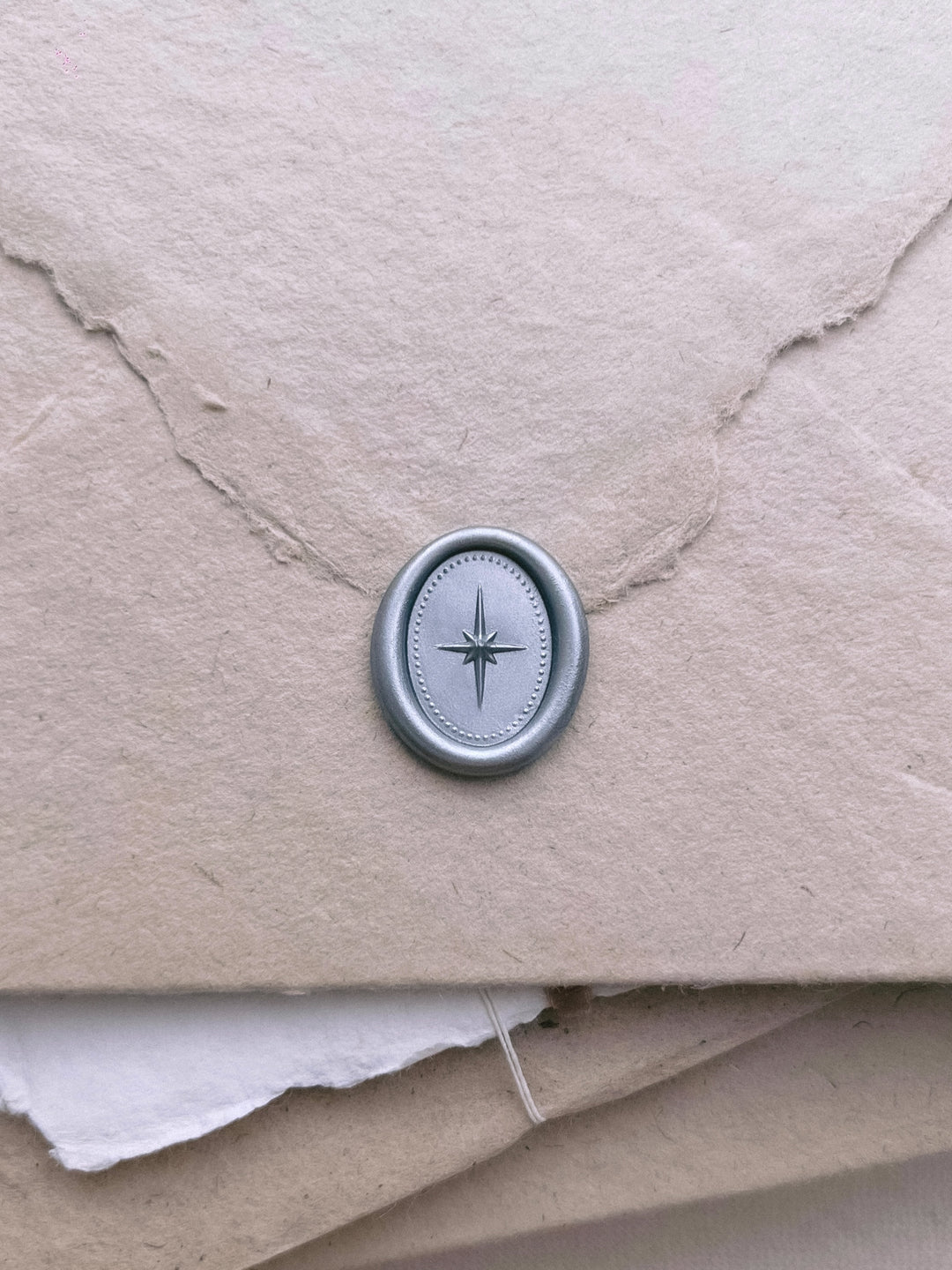 Silver 3D north star mini oval wax seal on a light brown textured handmade paper envelope