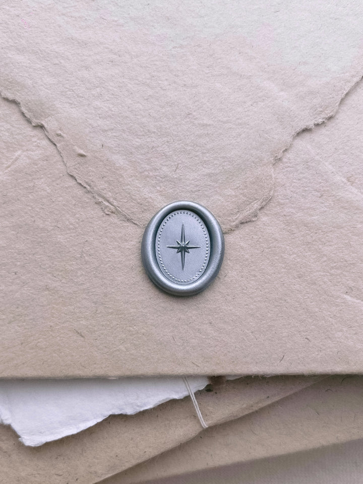 Silver 3D north star mini oval wax seal on a light brown textured handmade paper envelope