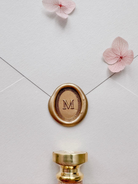 Gold mini oval monogram wax seal on a beige envelope styled with pink dried hydrangeas