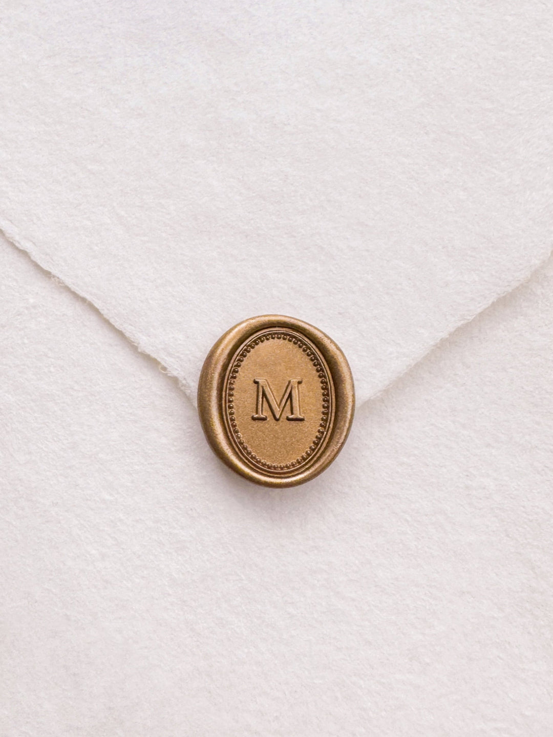 Gold mini oval letter wax seal on a white handmade paper envelope