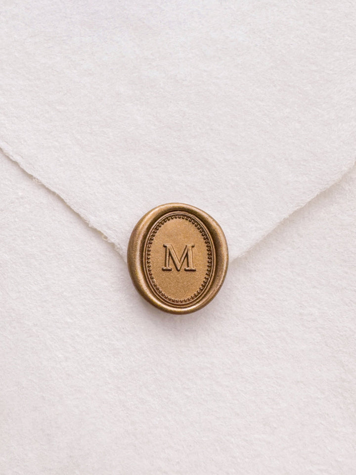 Gold mini oval letter wax seal on a white handmade paper envelope