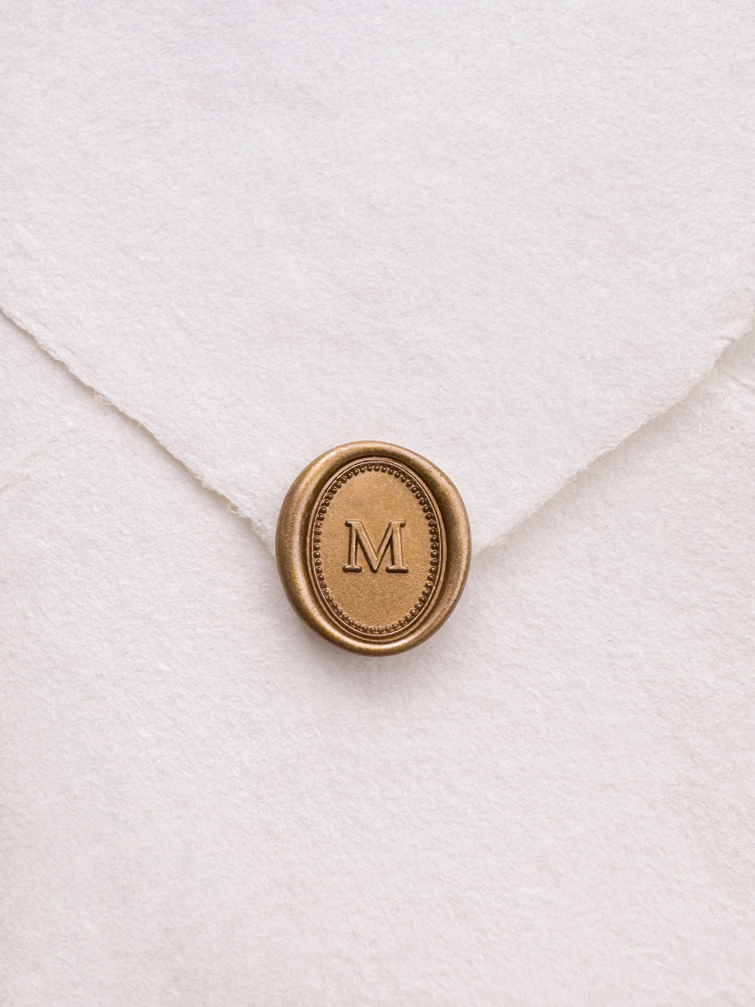 Personalized initial gold wax seal featuring a custom monogram with a dotted and line oval border design on a white textured envelope