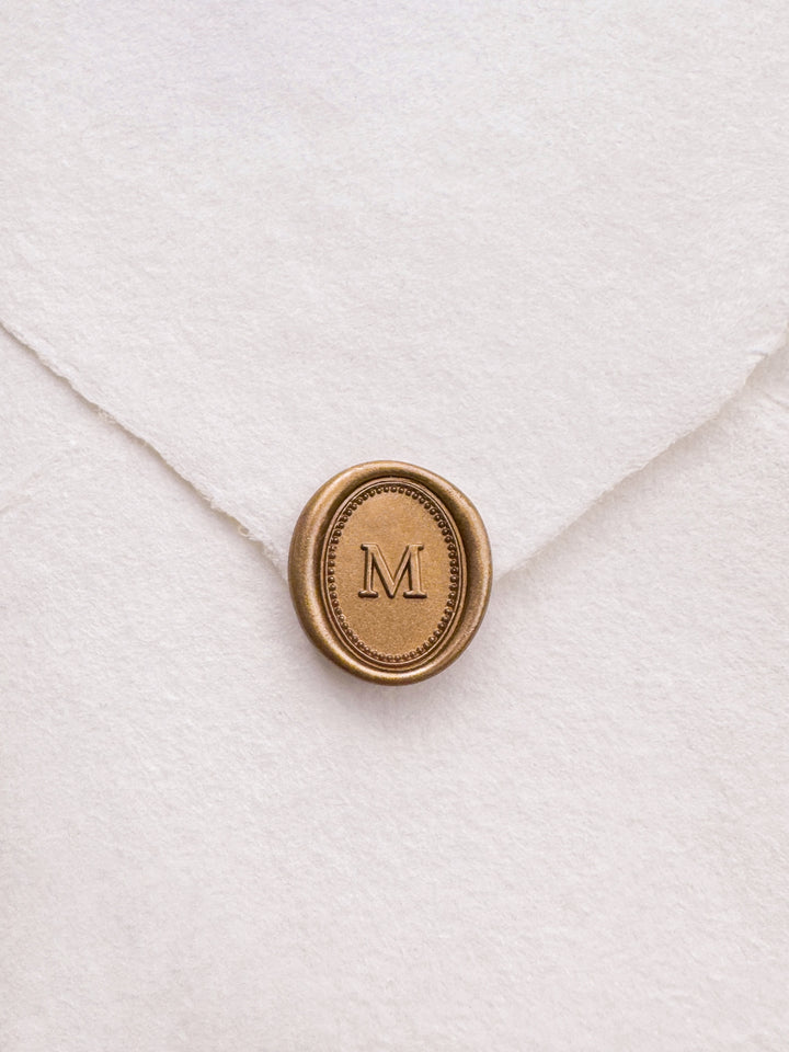 Personalized initial gold wax seal featuring a custom monogram with a dotted and line oval border design on a white textured envelope