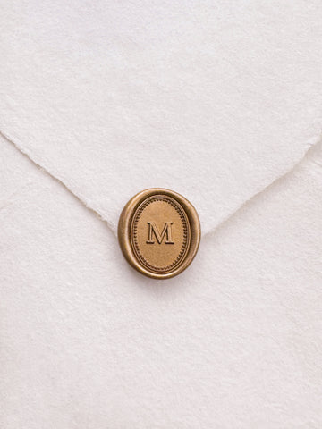 Gold mini oval letter wax seal on a white handmade paper envelope