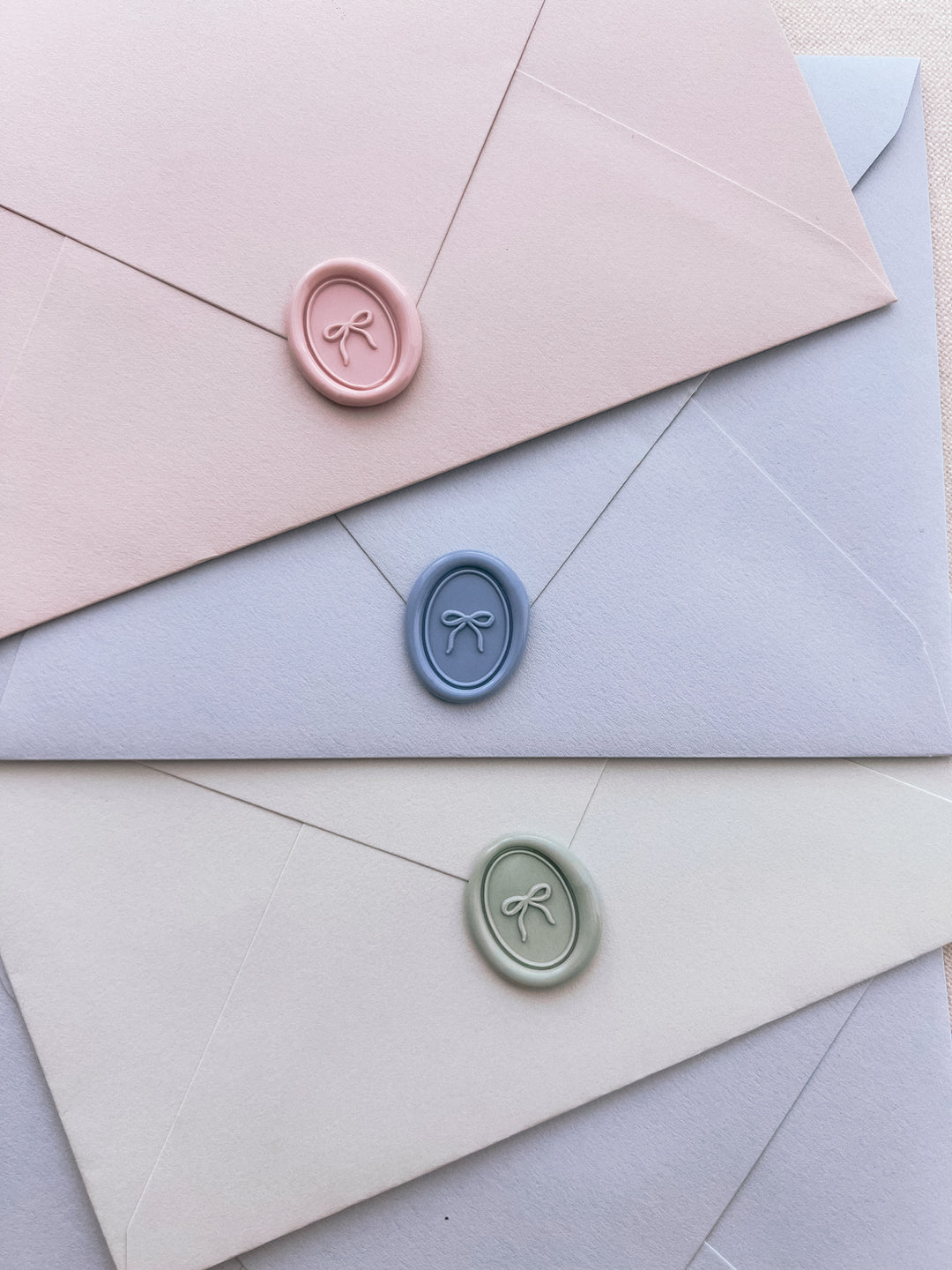 pink, dusty blue, and light sage green mini ribbon bow oval wax seals on pastel-toned envelopes