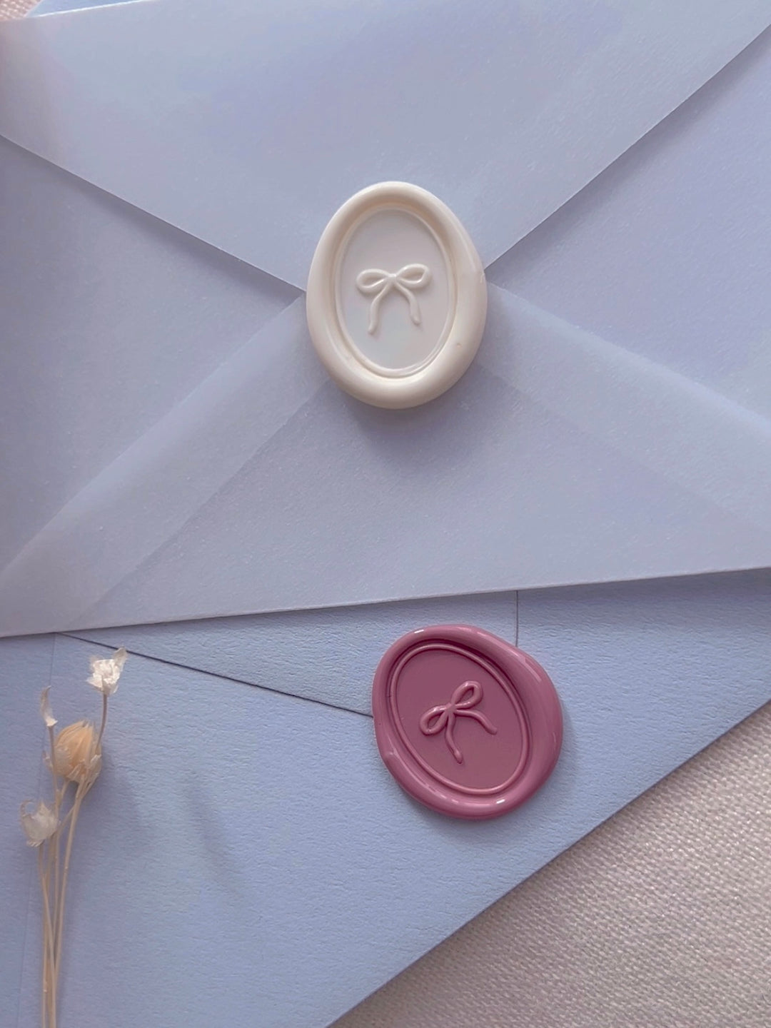 off-white and rose pink mini ribbon bow oval wax seals on a translucent vellum and light blue envelopes