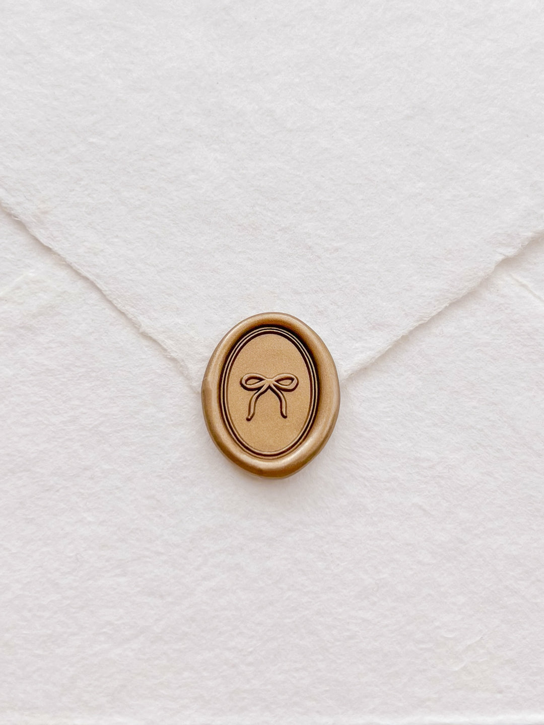 gold mini hand-drawn ribbon bow oval wax seal on a white deckle-edge handmade paper envelope
