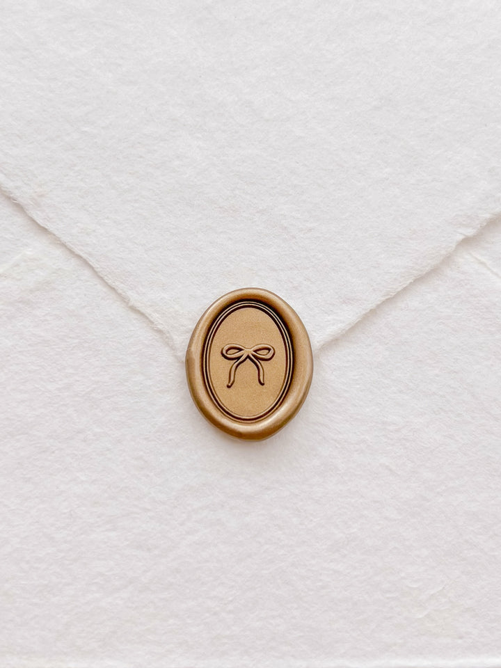 gold mini hand-drawn ribbon bow oval wax seal on a white deckle-edge handmade paper envelope