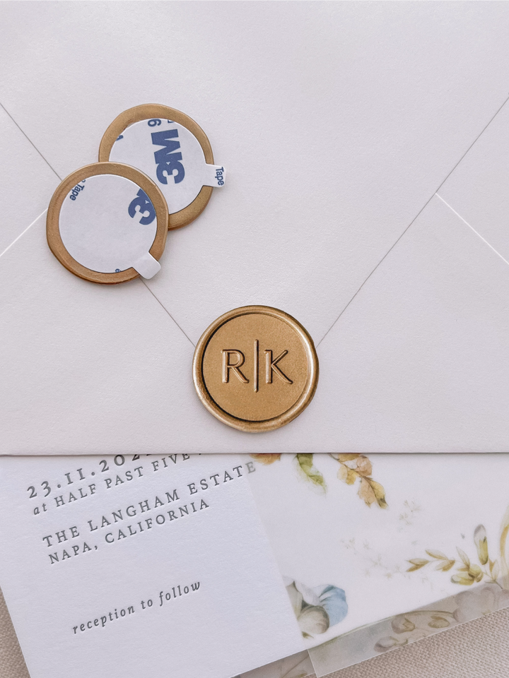 modern typeface monogram with "|" gold wax seal stickers with self-adhesive backings on a wedding invitation, beige envelope, and floral vellum jacket