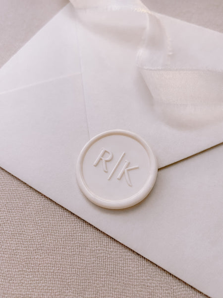 Modern typeface monogram custom wax seal in off-white on white paper envelopestyled with a strand of white silk ribbon