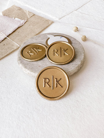 Modern typeface monogram custom wax seals in gold styled with a small gray stone dish, handmade paper and a dried floral branch
