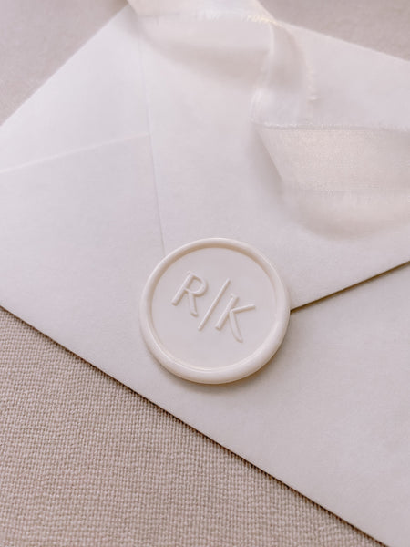 Modern typeface monogram off-white custom wax seal on paper envelope styled with a strand of white silk ribbon