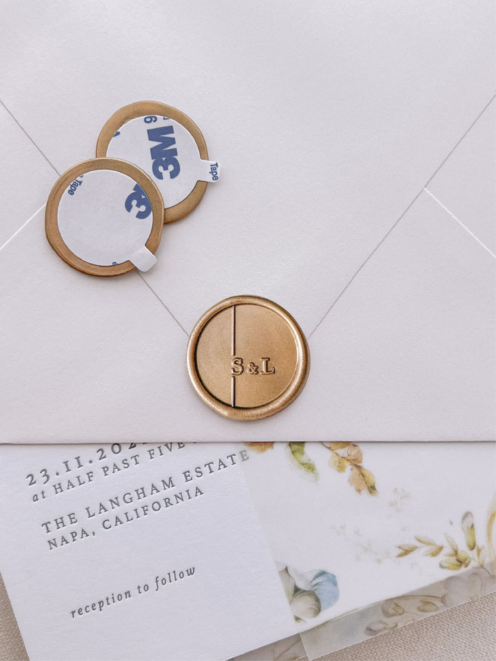 moderne monogram with "&amp;" gold wax seal stickers with self-adhesive backings on a wedding invitation, beige envelope, and floral vellum jacket