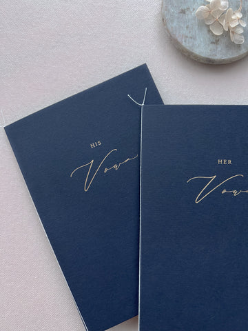 A set of two His and Her gold foil navy card stock vow books in calligraphy script tied with fine white twine