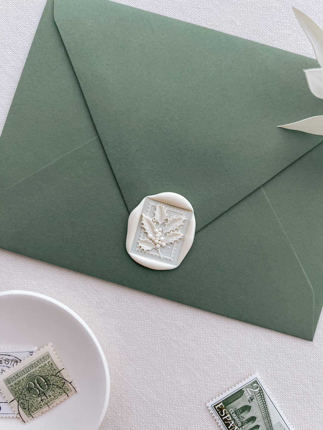 An off-white 3D Christmas holly rectangular wax seal on an olive green envelope