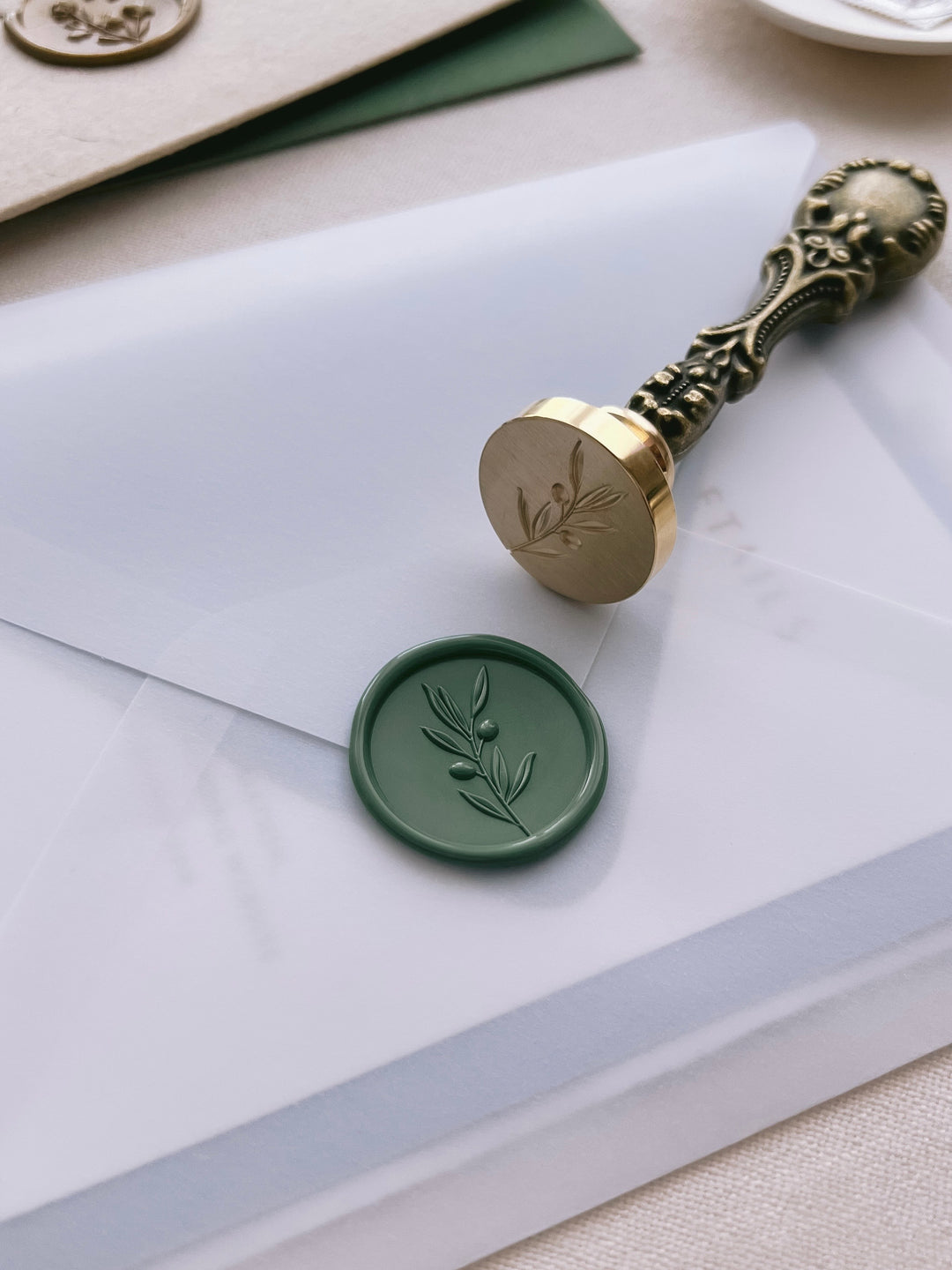 Green olive branch wax seal on a vellum envelope, with a wax seal stamp placed next to it