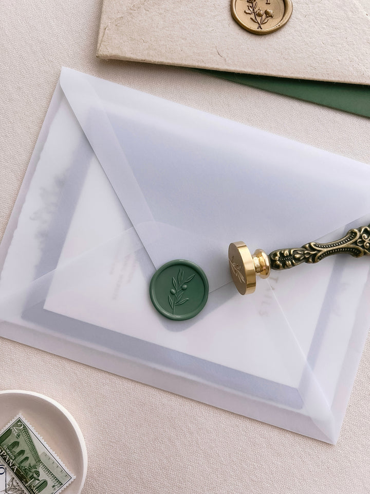 Green 3D olive leaf branch wax seal on a vellum envelope, with a wax seal stamp placed next to it