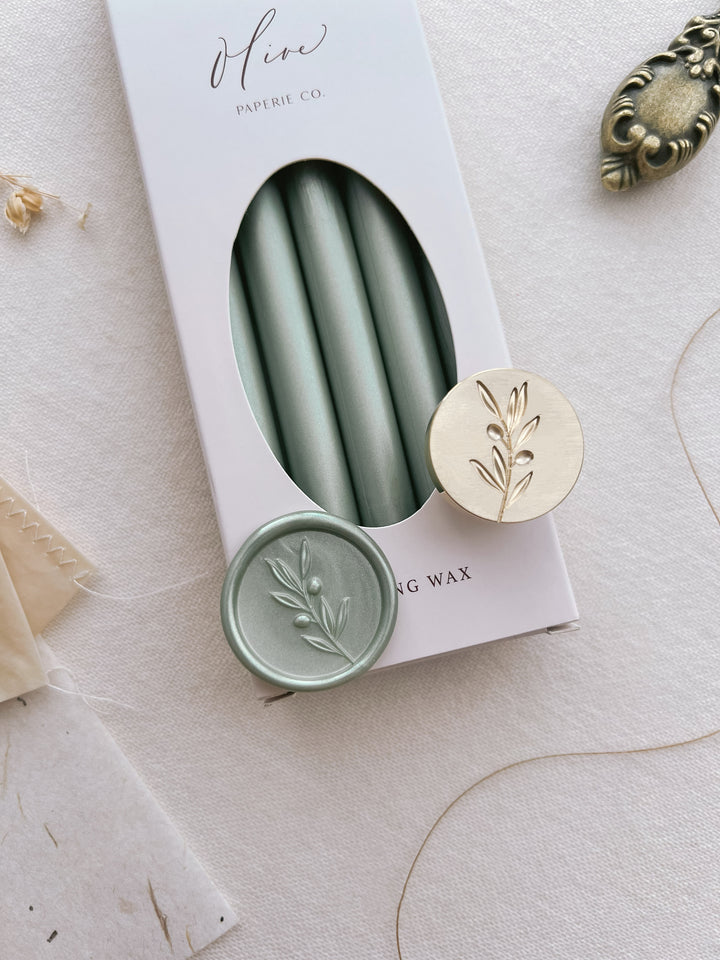 Light metallic sage green olive branch design wax seal on a box of metallic green sealing wax sticks 