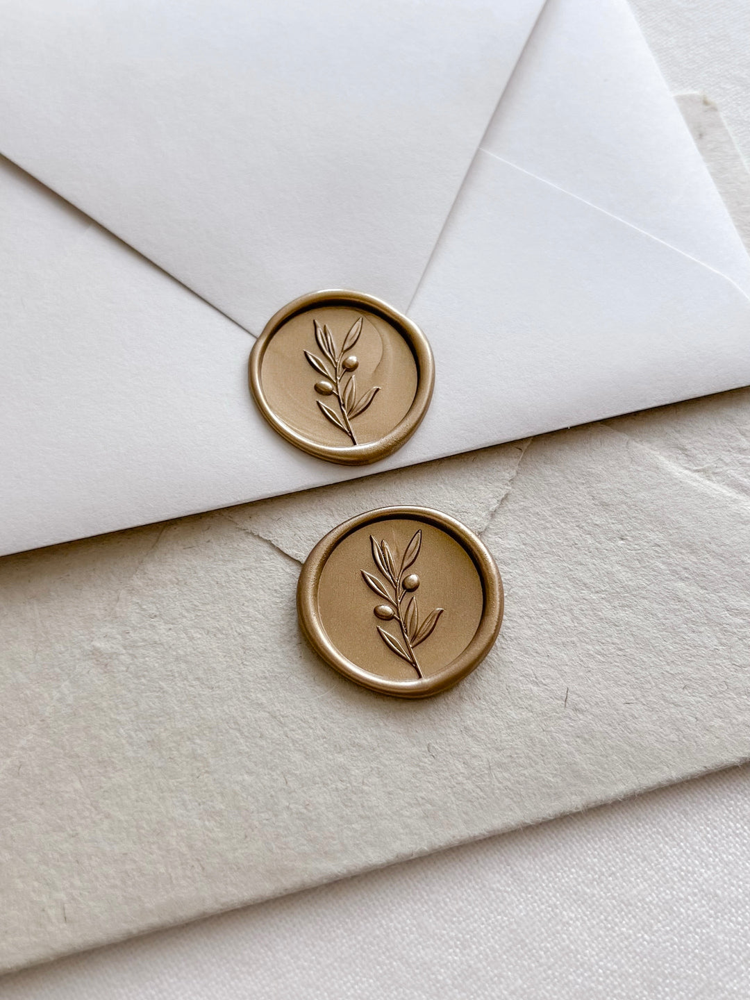 Gold colored 3D olive branch wax seals on white and light brown envelopes 