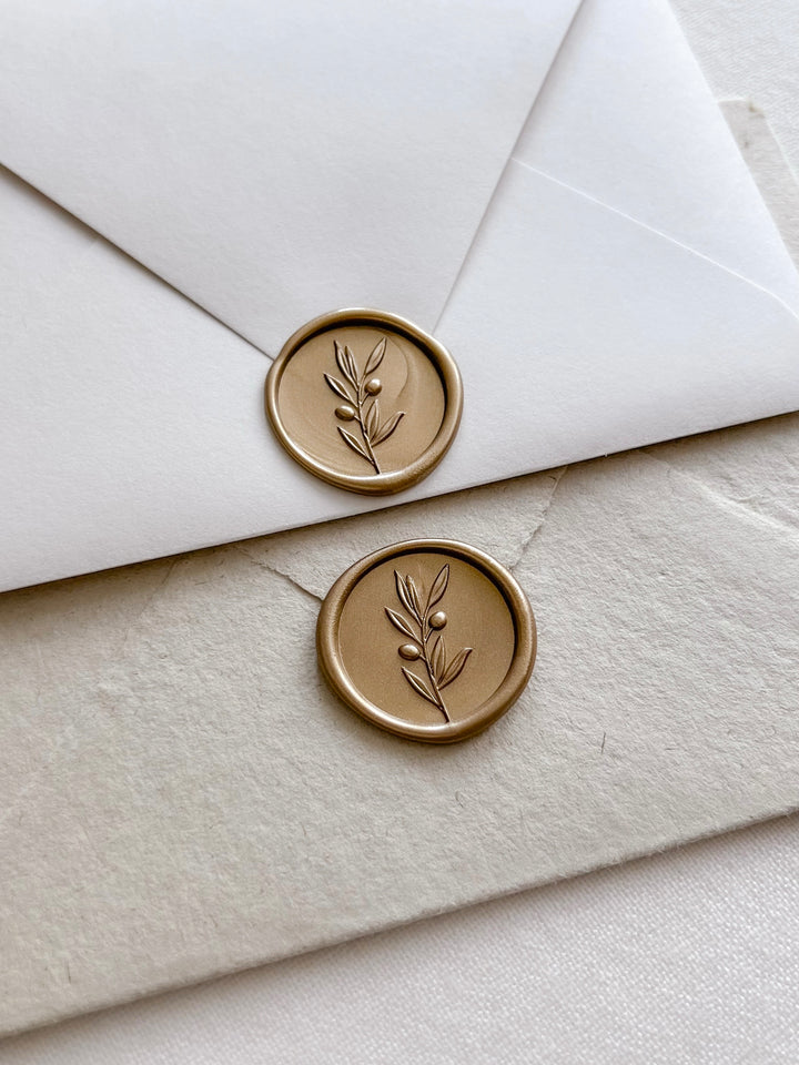 Gold colored 3D olive branch wax seals on white and light brown envelopes 