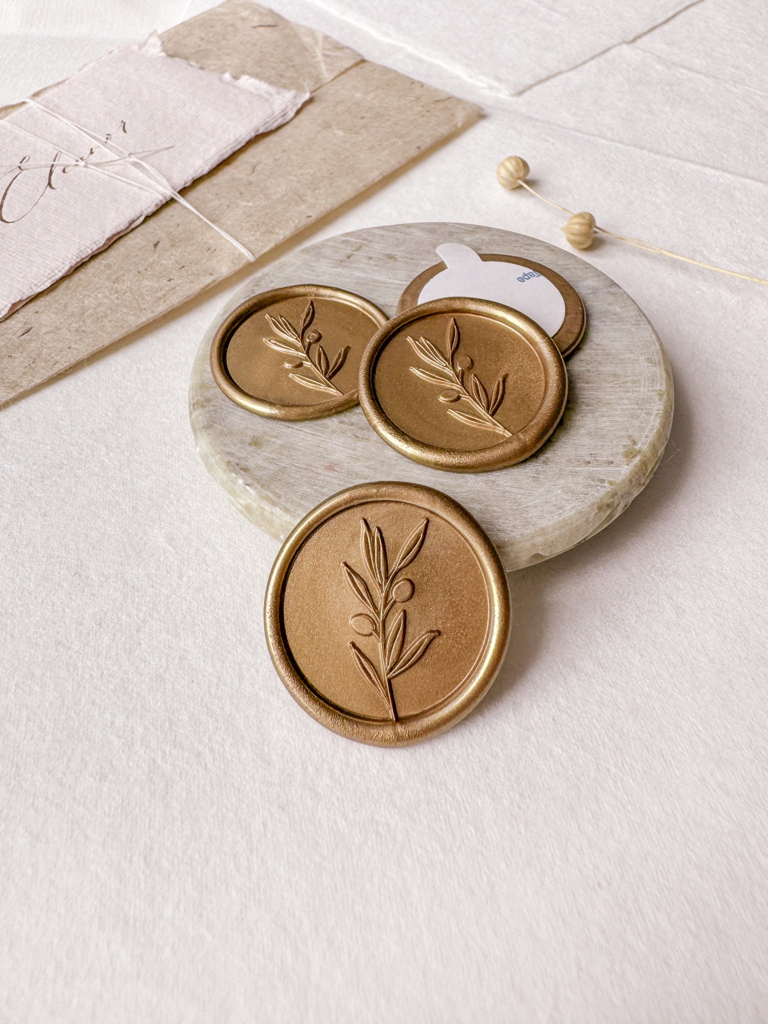 Olive branch gold wax seals styled with a small gray stone dish, handmade paper and a dried floral branch