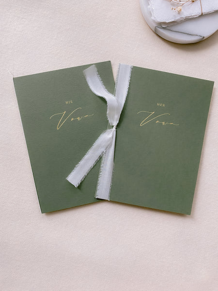 A set of two His and Her gold foil olive green card stock vow books in calligraphy script with one tied in white colored silk ribbon and the other in fine white twine