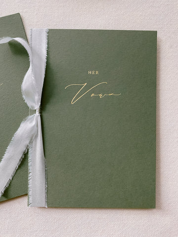 A set of two His and Her gold foil olive green card stock vow books in calligraphy script with antique white colored silk ribbon