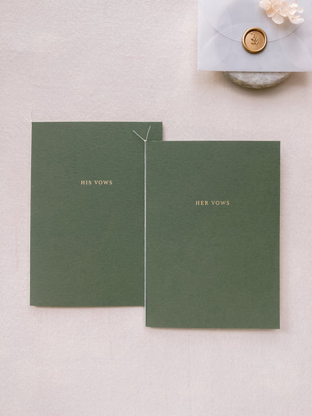 A set of two His and Her gold foil olive green card stock vow books in typeface font with fine white twine styled with small vellum envelop with mini leaf wax seal in gold