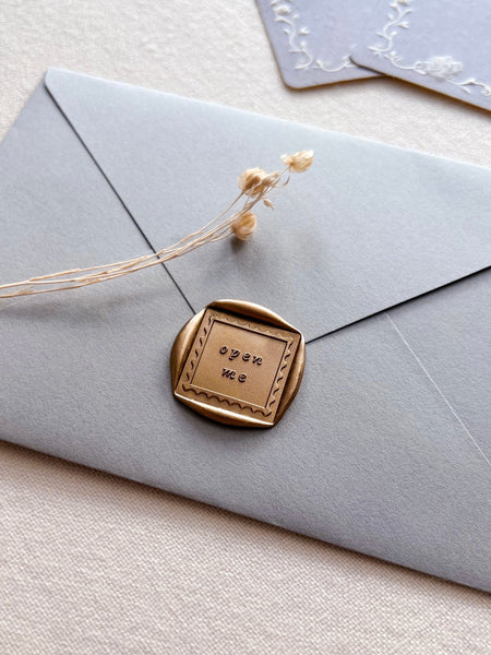 gold open me square wax seal on blue grey envelope