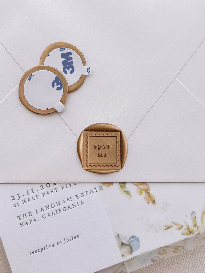 open me square gold wax seal stickers with self-adhesive backings on a wedding invitation, beige envelope, and floral vellum jacket