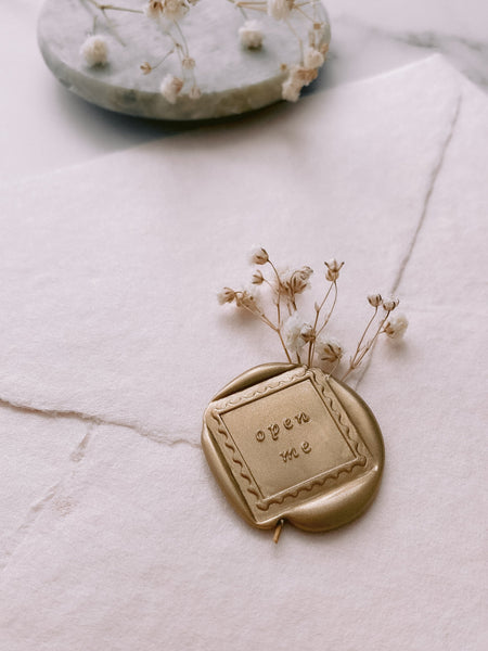 Open me wax seal in gold embellished with dried flowers on beige handmade paper envelope