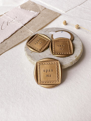 "open me" postage stamp design gold wax seals styled with a small gray stone dish, handmade paper and a dried floral branch