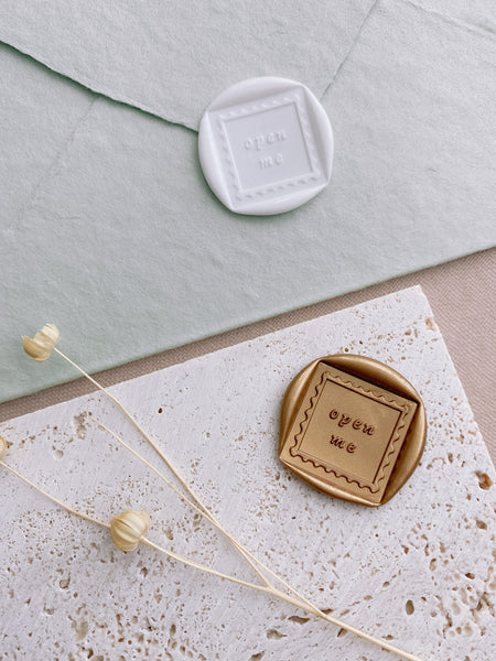 Open Me square shaped wax seals in white on handmade paper envelope and open me square shaped gold wax seal