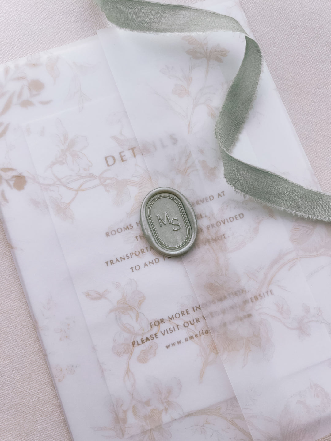 Light metallic sage green personalized initials oval arch wax seal featuring a custom monogram framed by simple double line border on a beige floral wedding invitation vellum jacket