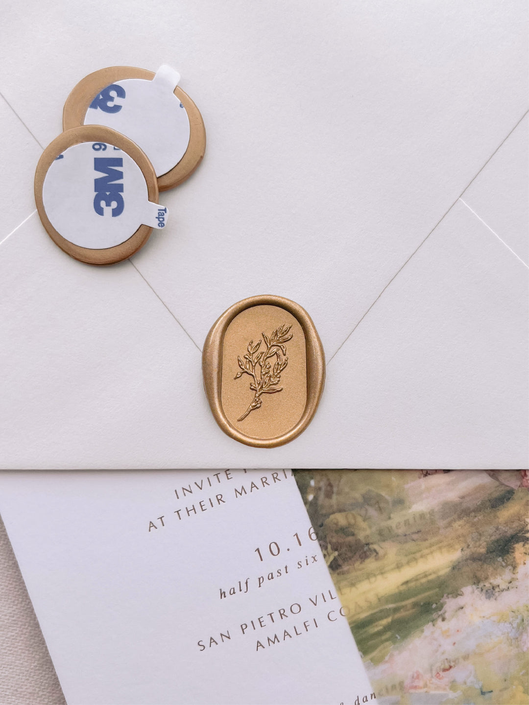 oval arch botanical gold wax seal stickers with self-adhesive backings on a wedding invitation, beige envelope, and floral vellum jacket