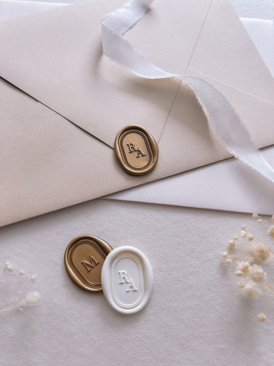 Personalized initials gold and white oval wax seals featuring a custom monogram and a simple line border on a stack of envelopes on a light beige background