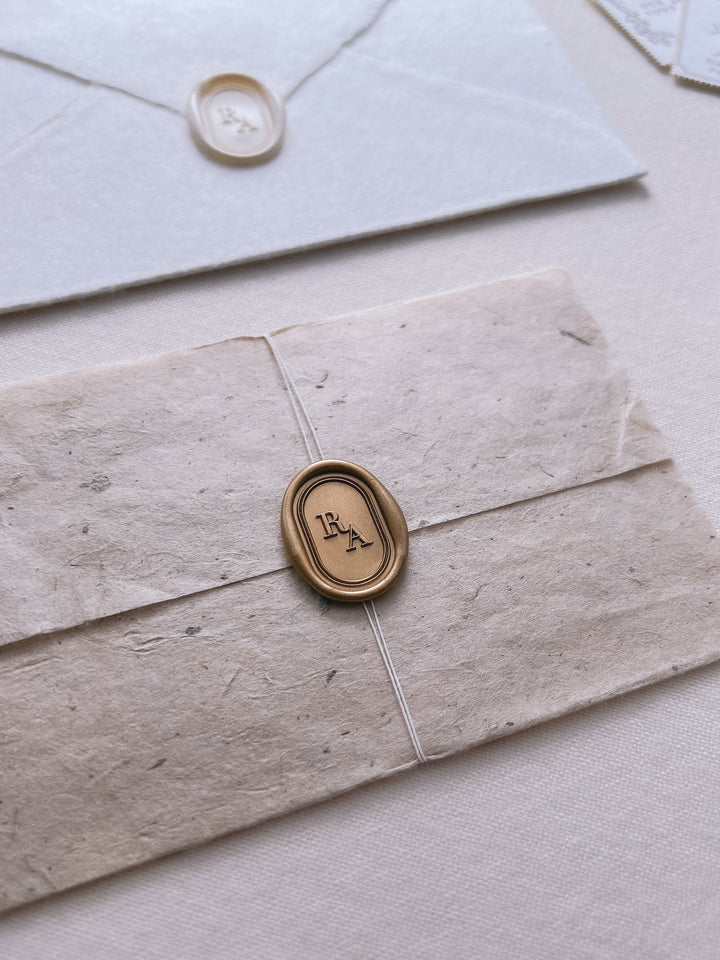 Personalized initials gold and white oval simple line border wax seals featuring a custom monogram on a white and light beige textured envelopes