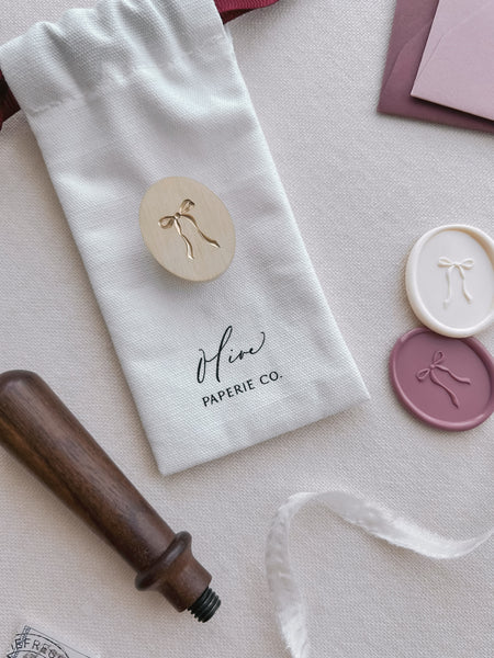 3D bow design oval wax stamp head and a walnut wooden stamp handle, with white and dusty rose colored bow design oval wax seals 