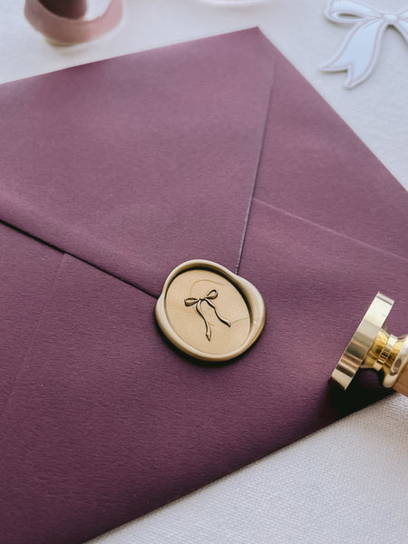 Burgundy envelope with a gold wax seal with a ribbon bow design