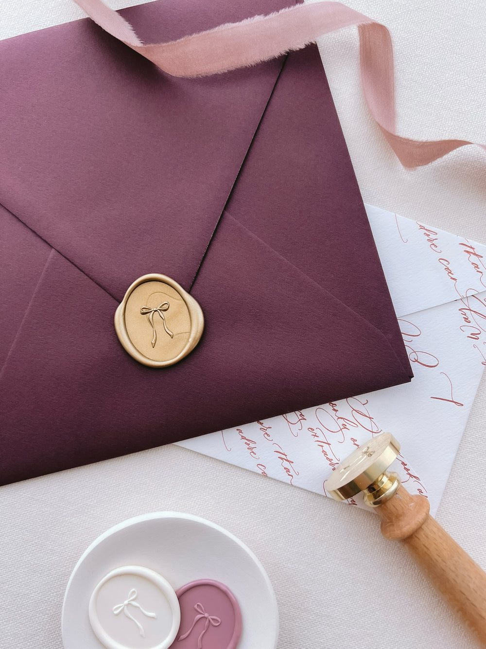 Burgundy envelope with a gold wax seal with a ribbon bow design