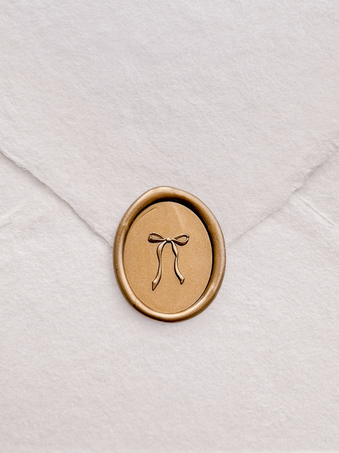 Gold ribbon bow oval wax seal with 3D engraving detail on a white textured handmade paper envelope 