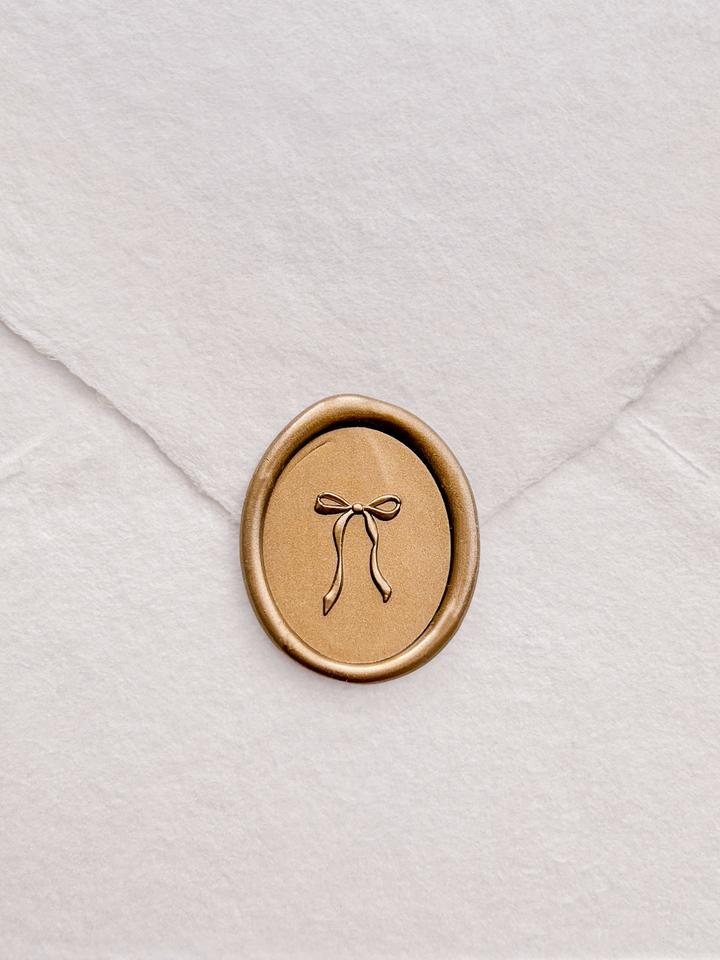 Gold ribbon bow oval wax seal with 3D engraving detail on a white textured handmade paper envelope 