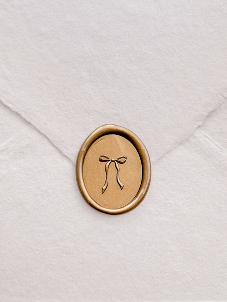 Gold oval wax seal with a bow design on a white envelope