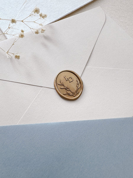 Oval leaf wreath custom initials gold wax seal on a beige envelope