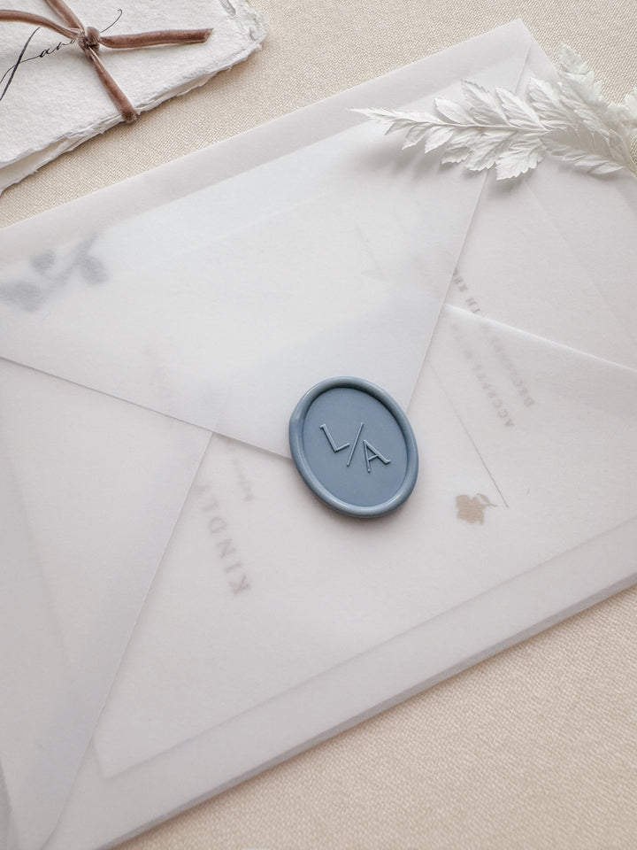 Dusty blue oval monogram wax seal on a wedding invitation vellum envelope